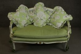 A French Louis XV style white painted and parcel gilt canape sofa, with a caned back, upholstered in