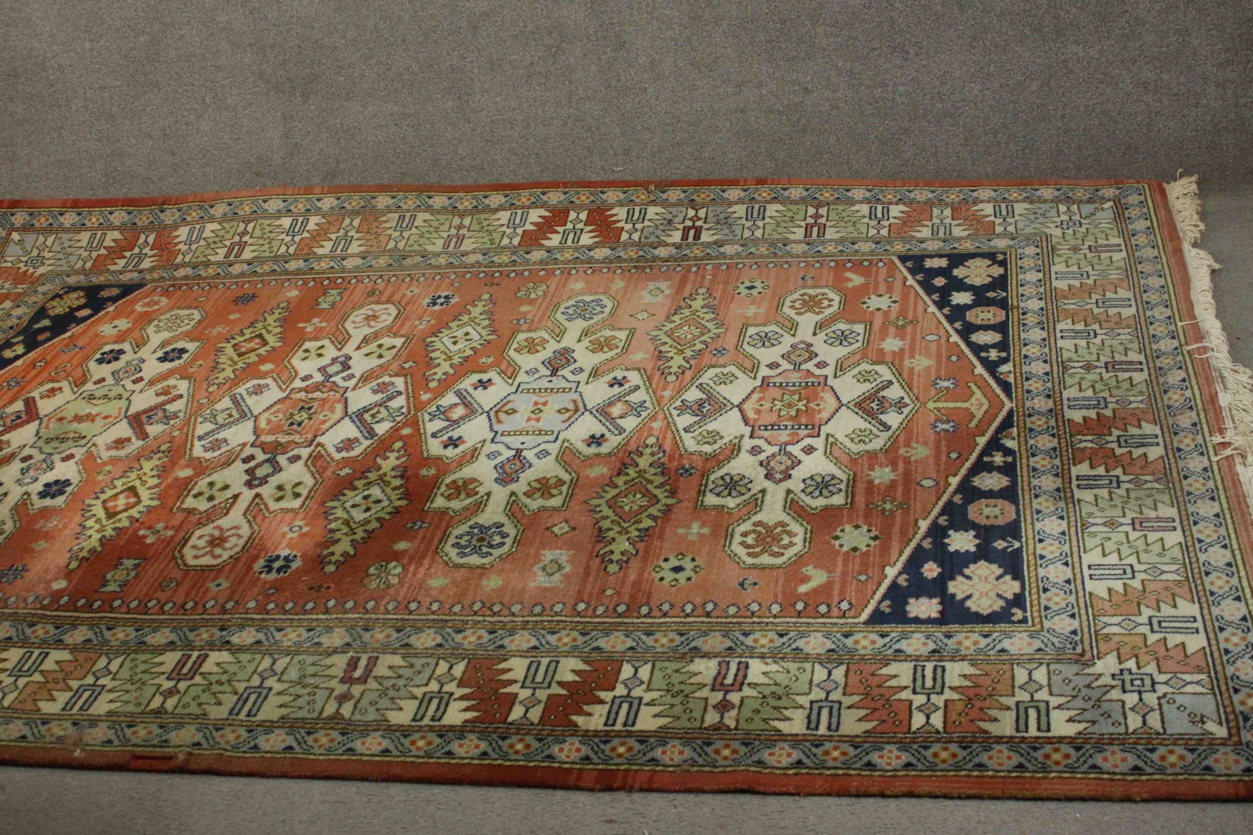 A Caucasian motif carpet with repeating stylised motifs on a terracotta field within geometric