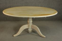 A cream painted and distressed oval dining table on a tripod base. H.77 W.158 D.105cm.
