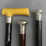Three old walking sticks, two with silver tops, one with a faux ivory handle and silver collar.