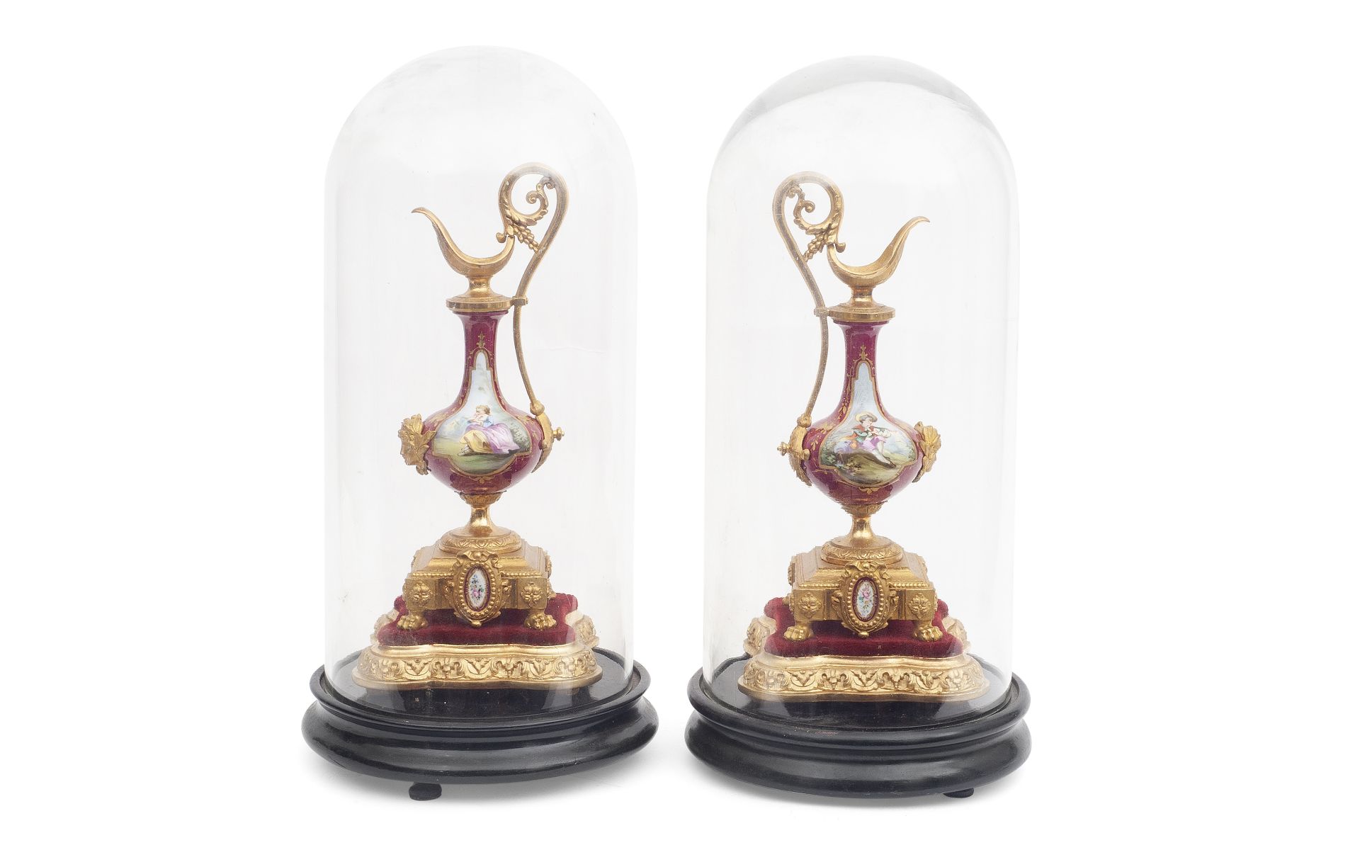 A PAIR OF GILT METAL AND PORCELAIN EWERS UNDER GLASS DOMES
