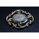 AN ANTIQUE MOURNING BROOCH, with black enamel, scrolling gilt metal surround and central oval