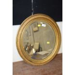 AN ANTIQUE GILT FRAMED OVAL BEVEL EDGED MIRROR - H 54 CM W 48 CM