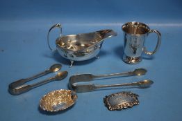 A HALLMARKED SILVER SAUCE BOAT, A MUG, PIN DISH AND BRANDY LABEL TOGETHER WITH PLATED SUGAR TONGS