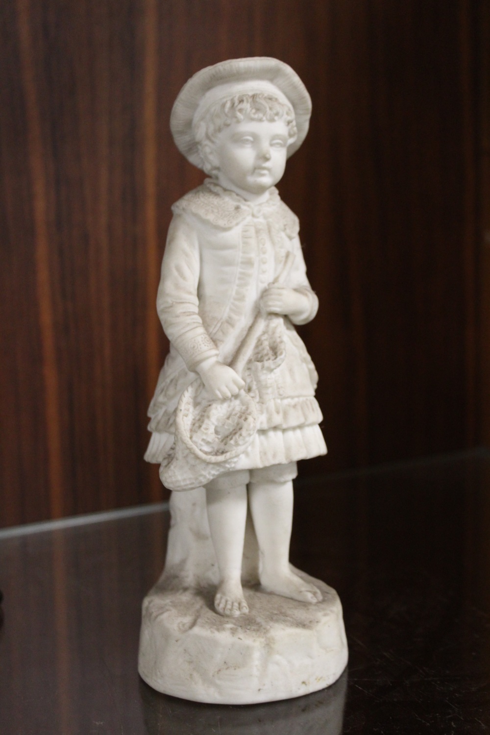 AN ANTIQUE MATTE FINISH FIGURE OF A YOUNG BOY IN A HAT MARKED R&L TO REVERSE H- 24CM