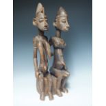 A TRIBAL ART CARVED WOODEN FIGURE DEPICTING A MAN AND A WOMAN SEATED, carved detail throughout, H 55