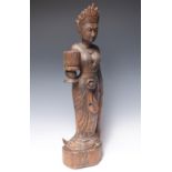 AN INDONESIAN CARVED HARDWOOD FIGURE OF A TEMPLE MAIDEN, in traditional dress, carrying a vessel