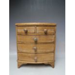 AN ANTIQUE PINE APPRENTICE BOW FRONTED CHEST OF DRAWERS, with five drawers, bun handles, raised on