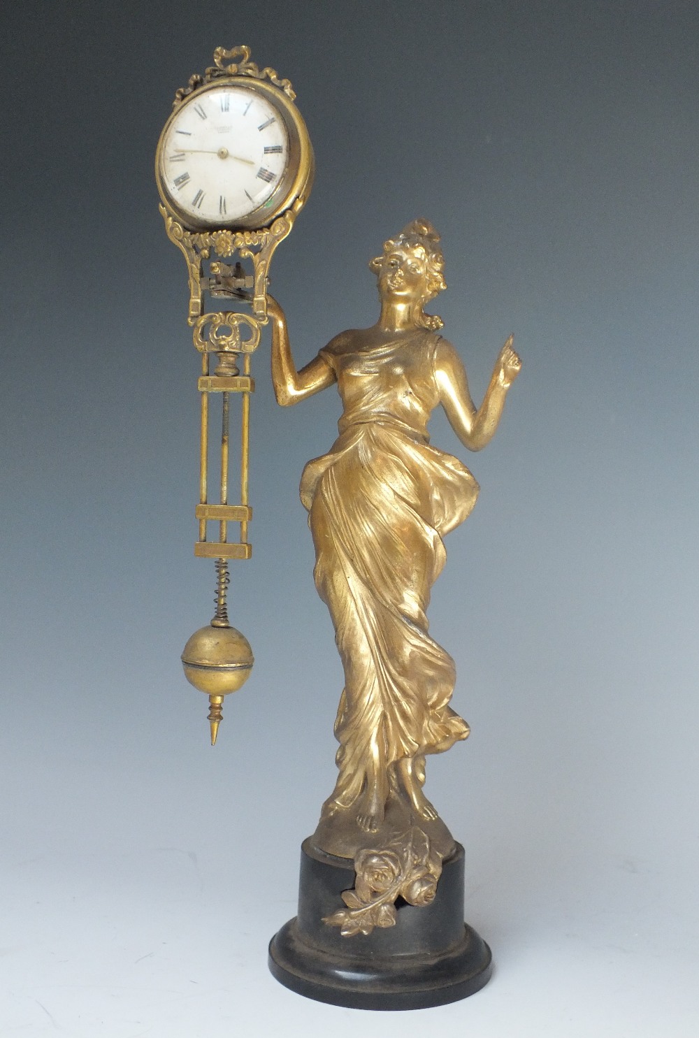 AN ART NOUVEAU FEMALE FIGURAL MYSTERY CLOCK, the gilded spelter figure with arm outstretched