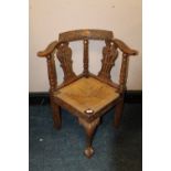 AN ANTIQUE OAK CARVED CORNER ARMCHAIR WITH DROP-IN WICKER SEAT