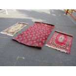 A RED AND BLACK WOOLLEN RUG AND TWO SMALLER EXAMPLES