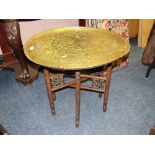 AN EASTERN BRASS TOPPED OCCASIONAL TABLE WITH TYPICAL FOLDING BASE