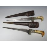 TWO 19TH CENTURY EASTERN DAGGERS IN LEATHER SHEATHS, the bone handles with white metal decorations