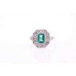 An emerald and diamond cluster ring, the emerald-cut emerald measuring 7.5x5mm with a weight of 0.