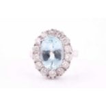 An aquamarine and diamond cluster ring, the oval faceted aquamarine within a surround of round cut