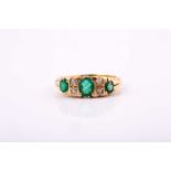 An 18ct yellow gold Edwardian ring set with ovalmixed cut emeralds, with the central emerald