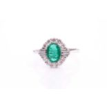 An Art Deco style emerald and diamond cluster ring, set with an oval emerald measuring 8x6mm of good