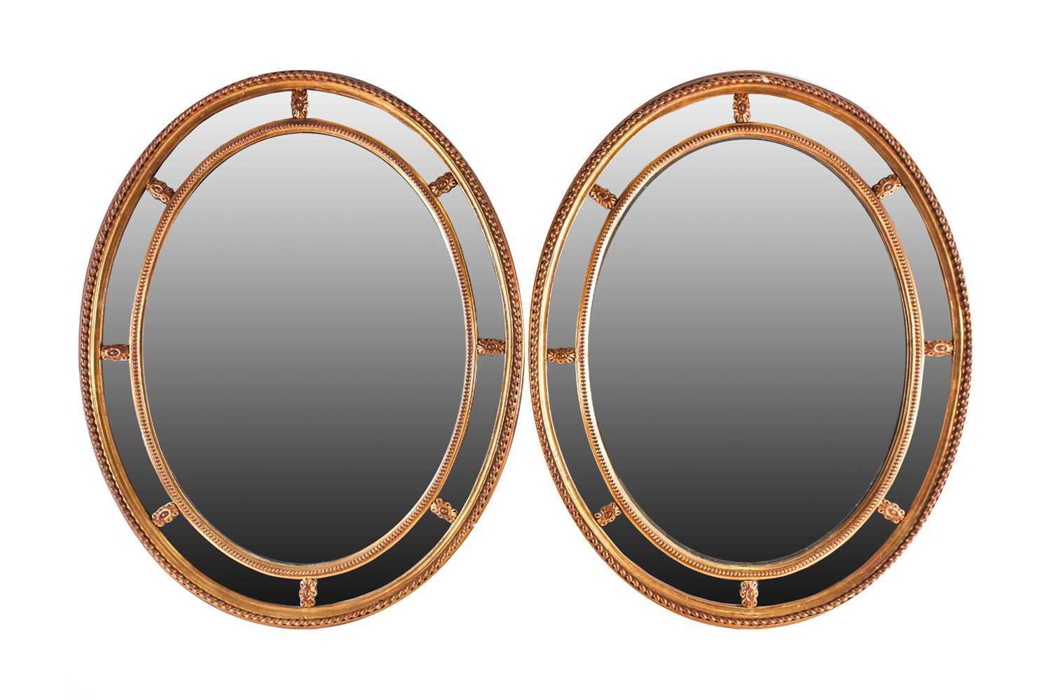 A pair of George III Adam style gilt framed oval mirrors, 20th century, with moulded paterae between