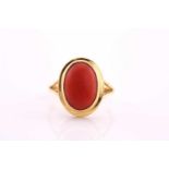 A coral cabochon ring, the 13.2 x 9mm oval cabochon to a yellow collet seIng and split shouldered