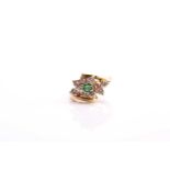 An emerald and diamond set cluster cross over ring, consisting of a central round emerald and ten-