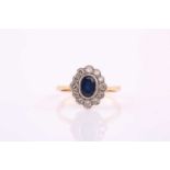 A sapphire and diamond cluster ring, the oval cut sapphire in rub-over setting, within a border of