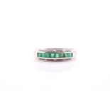 An emerald and diamond half hoop eternity ring; the central band of calibré cut emeralds within