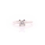 A single stone diamond ring; the princess cut diamond in raised four claw mount to a plain white