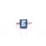 A topaz and diamond ring; the cut-cornered step cut blue topaz in four claw mount; to five stone