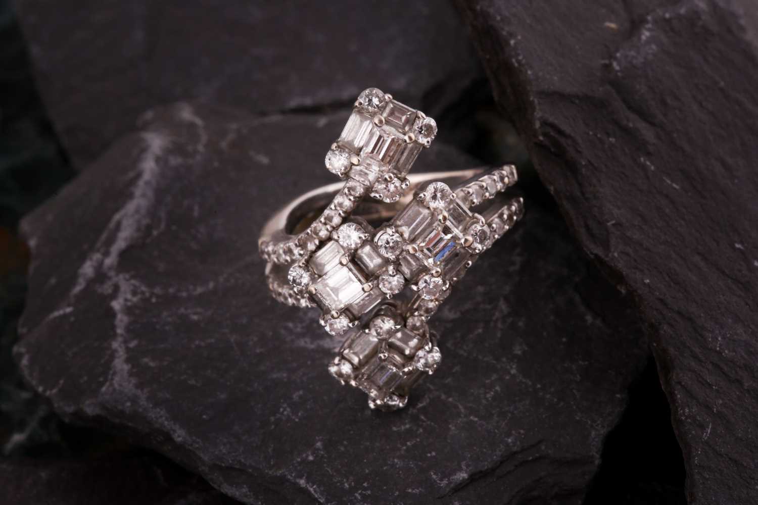 A diamond dress ring Of bifurcated design, obliquely-set to the front with four clusters of baguette