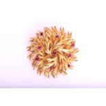 A 9ct gold brooch of round textured organic form claw set with eight round mixed cut rubies, 4cm