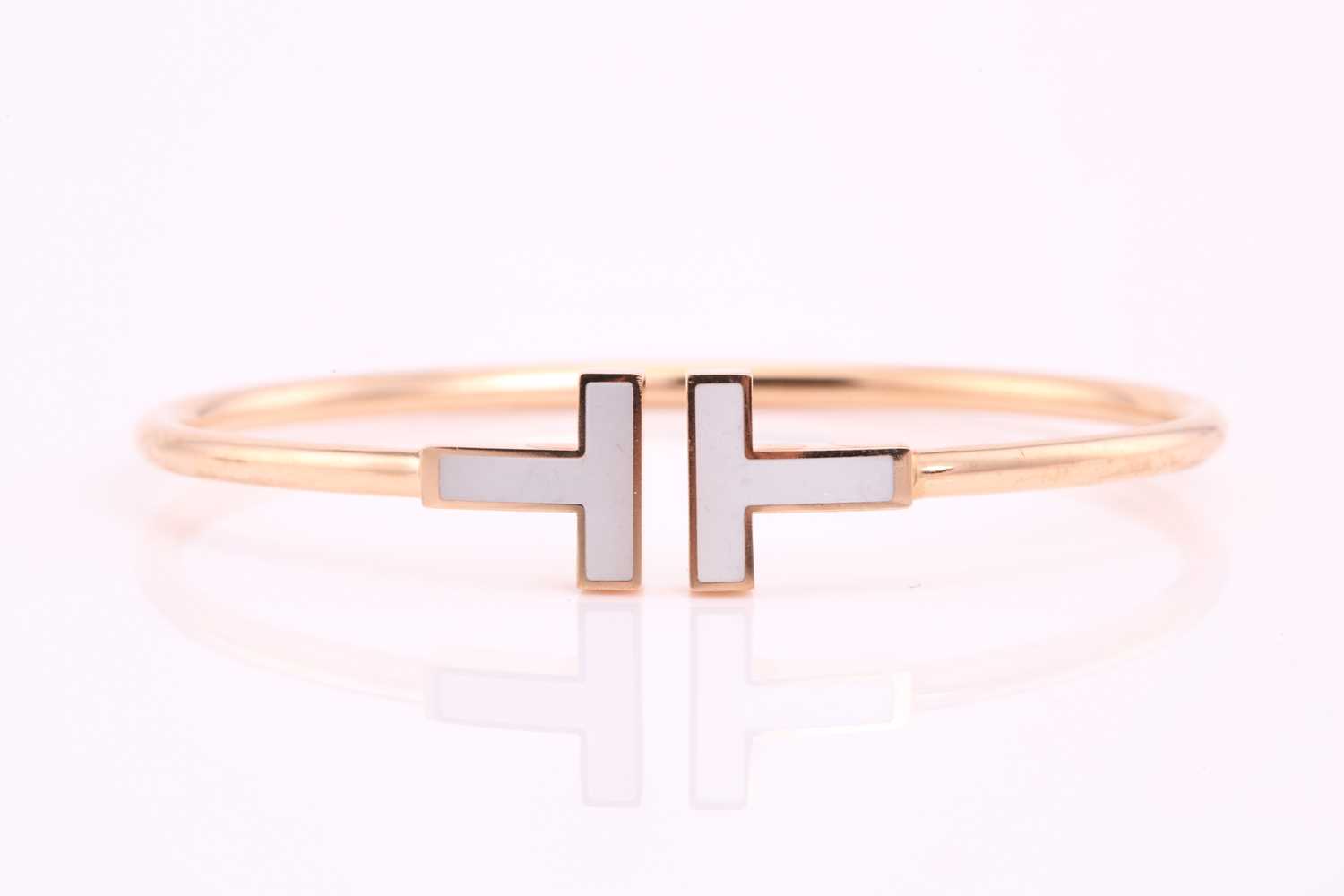 Tiffany. A gold and mother of pearl T wire bangle; 18 carat gold with mother of pearl T terminals.