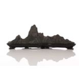 A Chinese carved and part polished stone brush rest, of mountain form with six peaks, on fitted wood