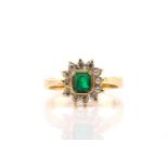 An emerald and diamond cluster ring, featuring an emerald with an intense green colour collet set in