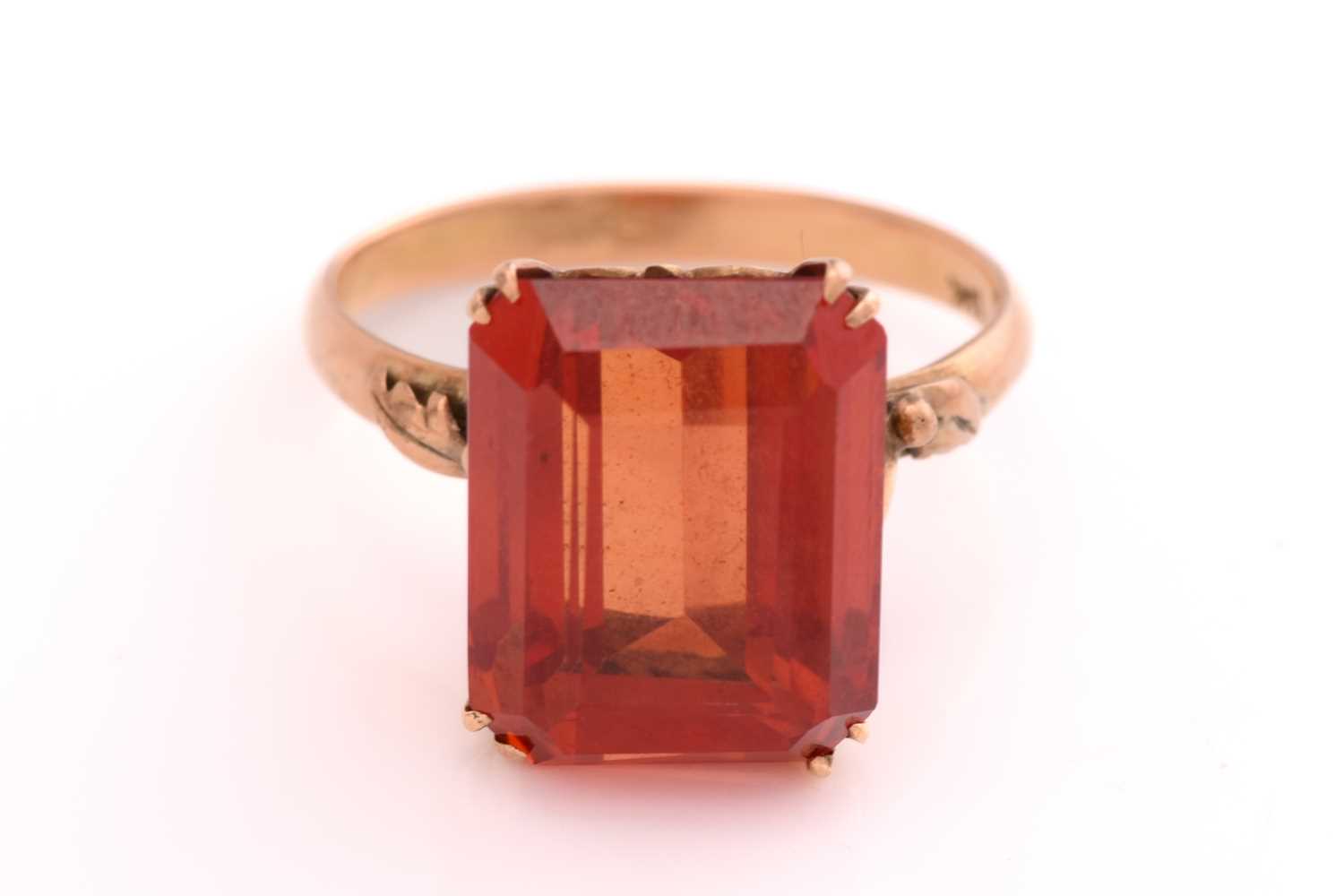 A synthetic orange sapphire ring, with an emerald-cut synthetic sapphire in reddish-orange colour,