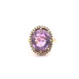 An amethyst and diamond halo ring, consisting of an oval mixed-cut amethyst in pinkish-purple