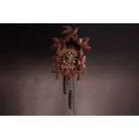 An early 20th century carved walnut cuckoo wall clock with a pair of cast pine cone weights and leaf