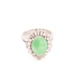 A jade and diamond entourage ring, consisting of an oval jadeite cabochon, in mottled bluish-green