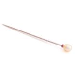 A pearl stick pin, the egg-shaped pearl has cream overtones, sits above a faceted ruby rondelle,