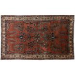 An old silk Kashan rug with stylized shrubs and flowers on a dark brick red ground, within