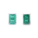 A pair of emerald stud earrings, each comprising a rectangular emerald-cut emerald with intense