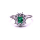 An emerald and diamond entourage ring in 18ct white gold, featuring an emerald-cut emerald of 4.9