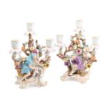 A pair of Meissen three branch candelabra, depicting a figure seated with a spilling bag of gold and