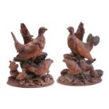 A pair of Black Forest carved wood figures of partridges, with their offspring, on ivy-carved