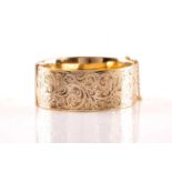 A 9ct yellow gold hinged bangle, the hollow bracelet is engraved with scrollwork design, completed