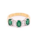 An emerald and diamond dress ring in 18ct bi-coloured gold, comprising three oval-cut emeralds in