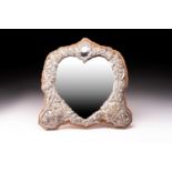 A heart-shaped silver frame dressing table mirror; in late 19th-century taste and chased with putti,
