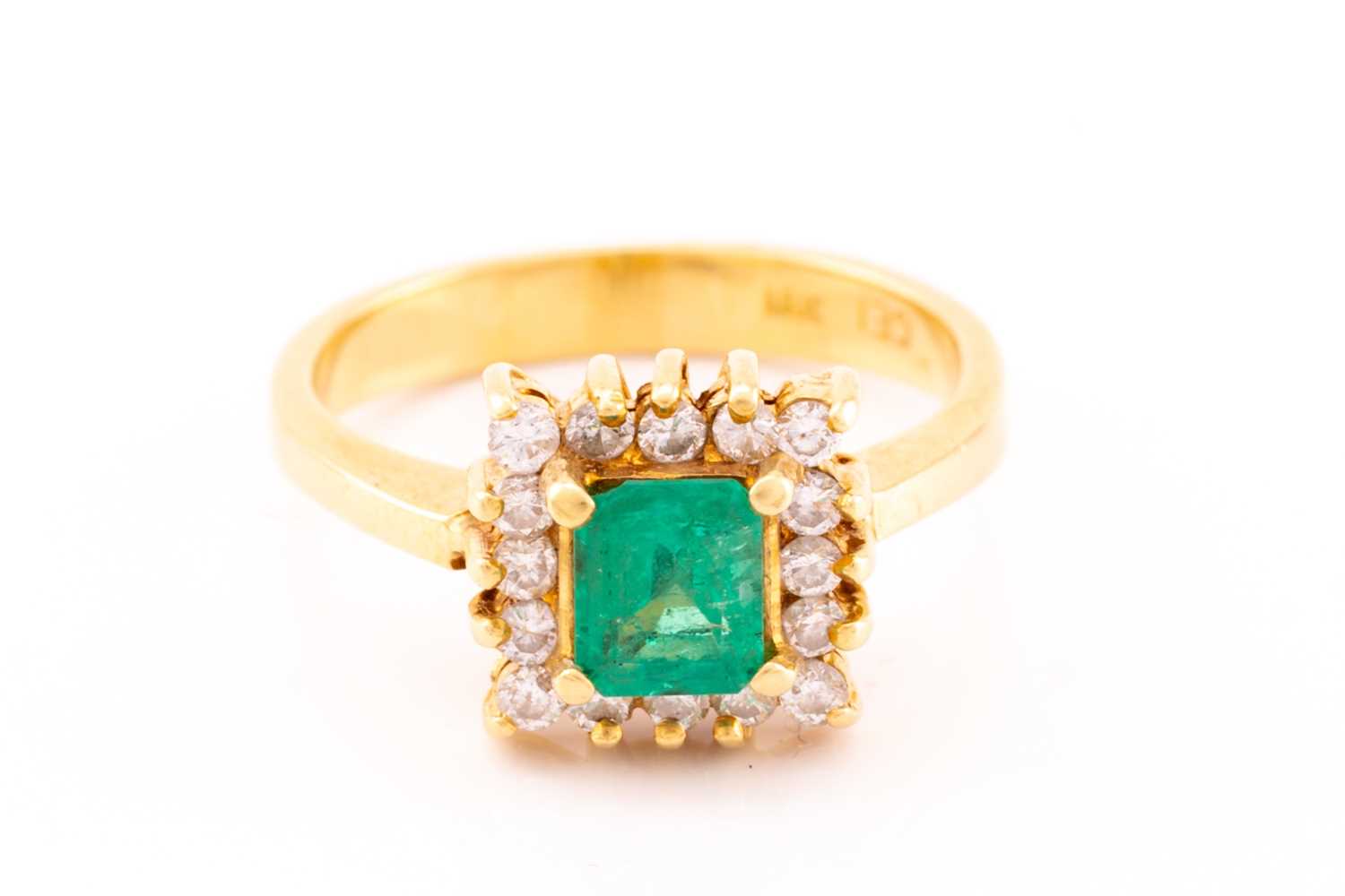 An emerald and diamond entourage ring, centred with an emerald-cut emerald in bright green colour,