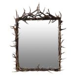 A LARGE AND ORNATE ANTLER MIRROR, comprising a large plate surrounded by an arrangement of red