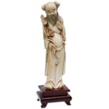 A LARGE CHINESE IVORY CARVING OF AN IMMORTAL, holding a lotus flower mounted on a stained wooden