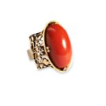 AN ARTS AND CRAFTS CORAL AND GOLD RING the oval cabochon-cut coral, four double claw set on an